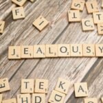 Wooden Scrabble letter tiles forming the word 'Jealousy' on a rustic wooden surface.