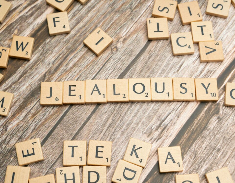 Wooden Scrabble letter tiles forming the word 'Jealousy' on a rustic wooden surface.