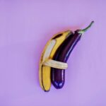A vibrant and artistic arrangement of a banana and eggplant against a violet backdrop, highlighting color and freshness.