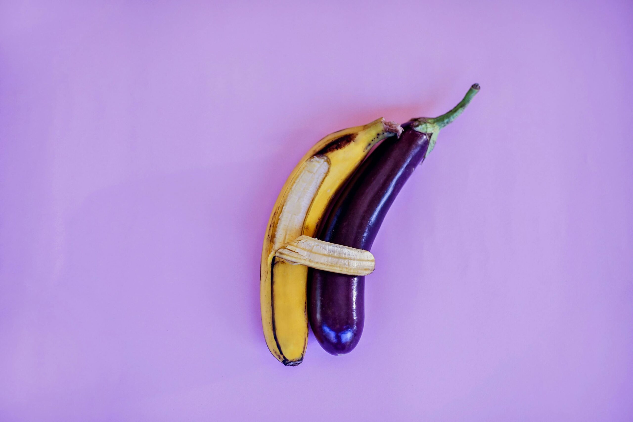 A vibrant and artistic arrangement of a banana and eggplant against a violet backdrop, highlighting color and freshness.