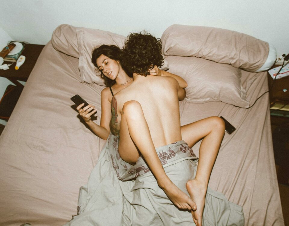 A couple in bed looking at smartphones, highlighting modern disconnection.