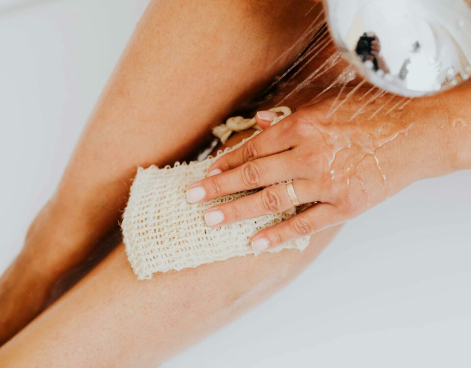 Close-up of a person exfoliating legs in the shower with a body scrubber.