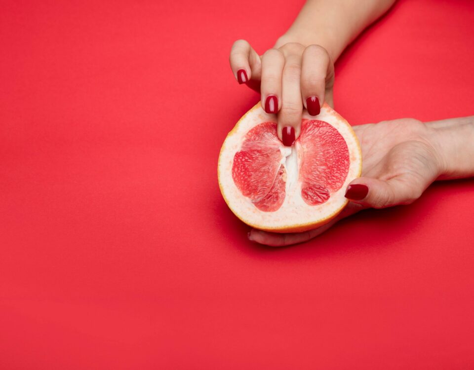 Close-up view of a hand with red nails holding a grapefruit against a red background. Symbolic and abstract.