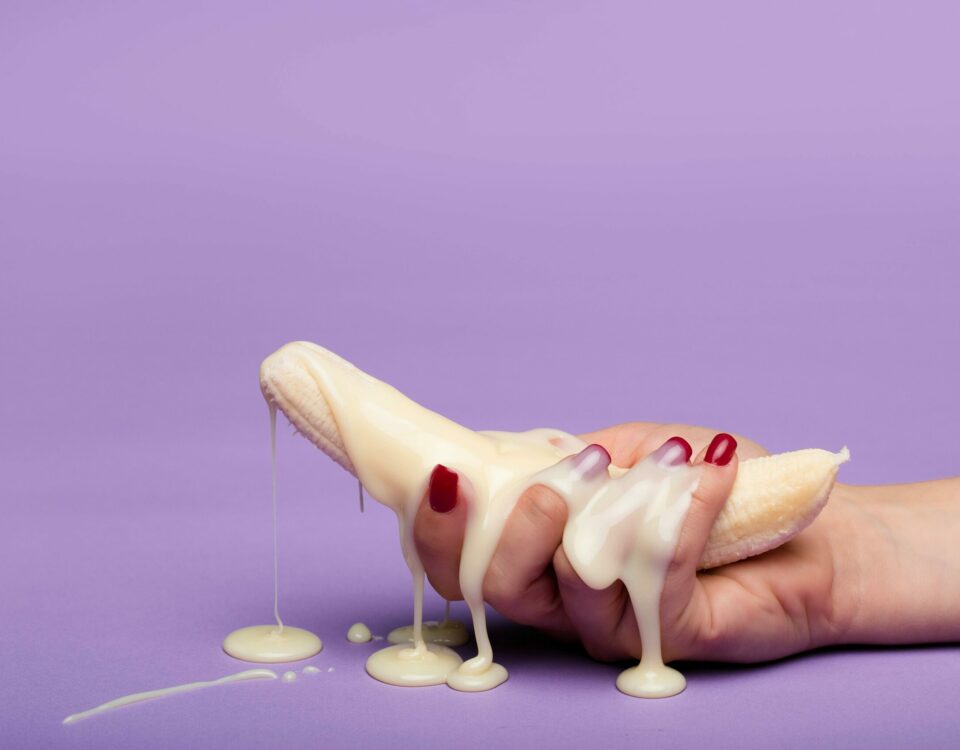 Creative conceptual image of a banana with cream on a purple backdrop, symbolizing indulgence.