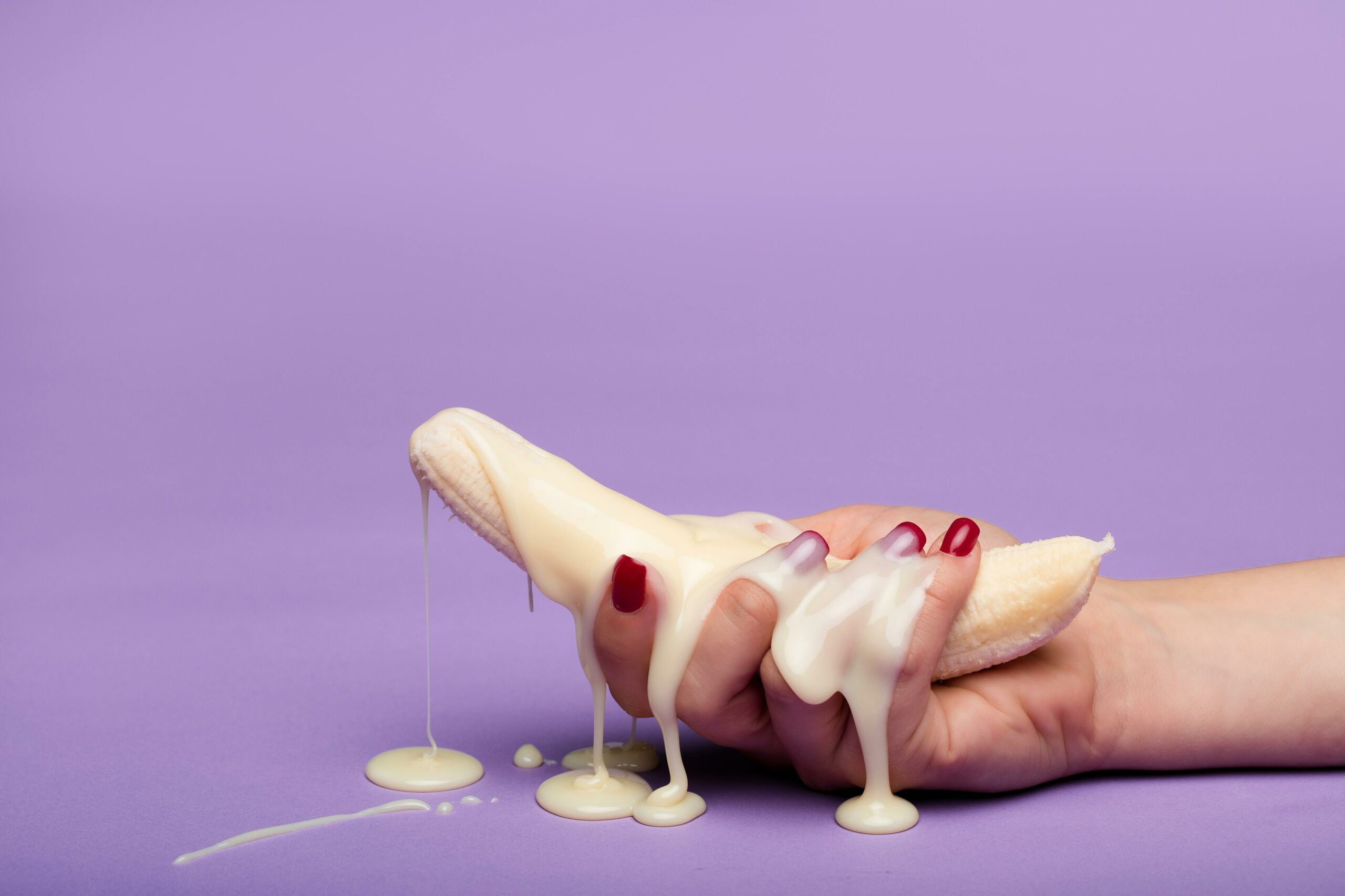Creative conceptual image of a banana with cream on a purple backdrop, symbolizing indulgence.