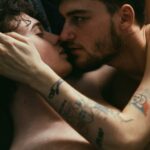 Tender moment between two young men embracing in bed, expressing intimacy and love.