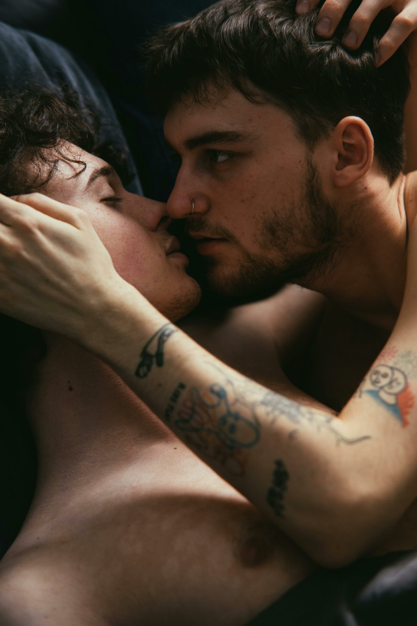 Tender moment between two young men embracing in bed, expressing intimacy and love.