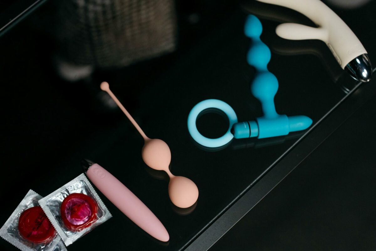 A collection of various sex toys and condoms on a reflective tabletop for safe and sensual pleasure.