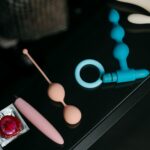 A collection of various sex toys and condoms on a reflective tabletop for safe and sensual pleasure.