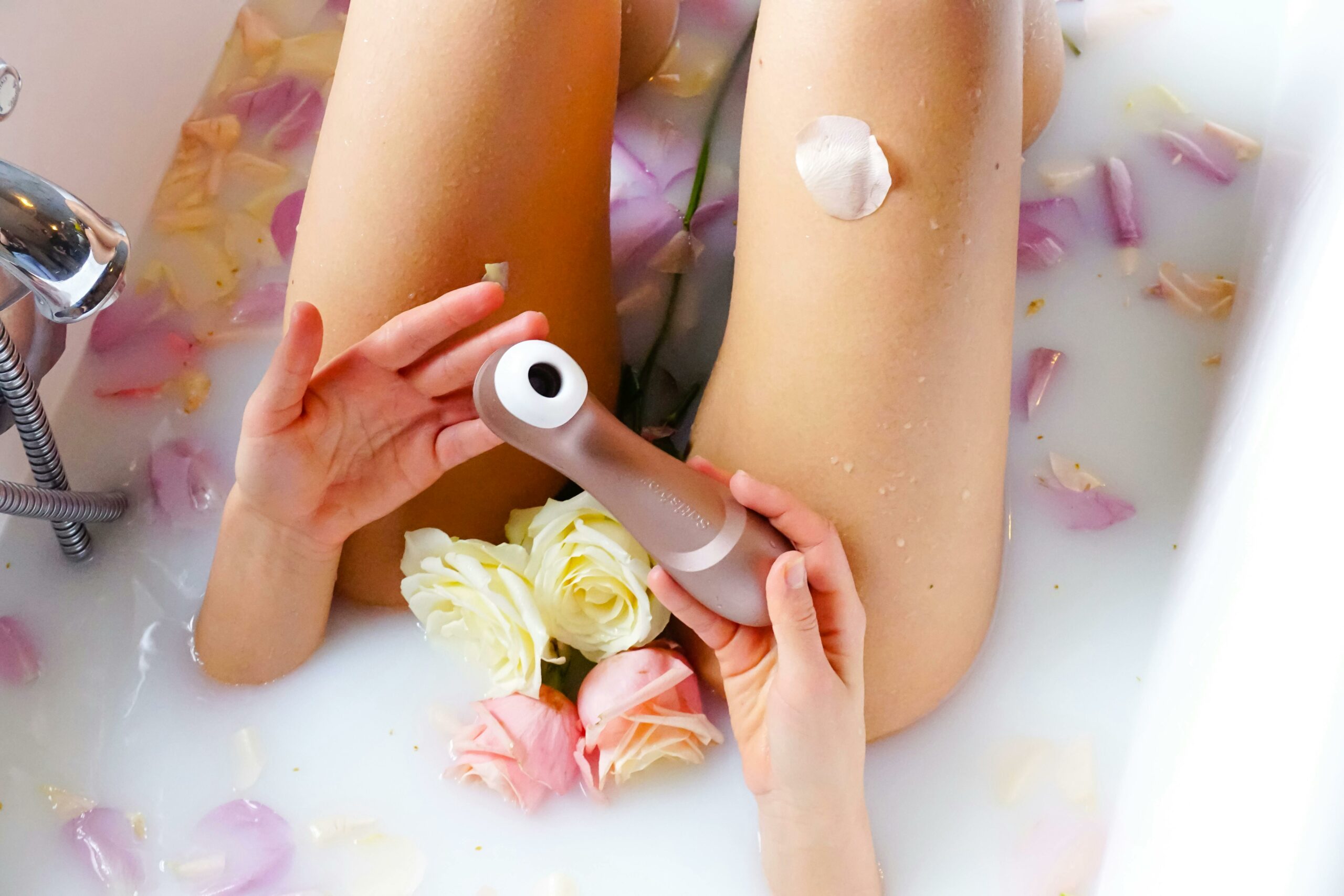 A serene bathtub scene with rose petals and a self-care device, promoting relaxation and sensuality.