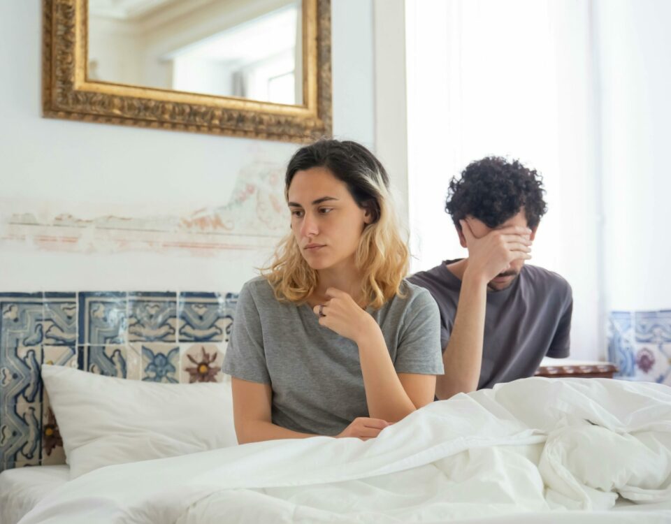 A couple sits together in a bedroom, experiencing a moment of misunderstanding.
