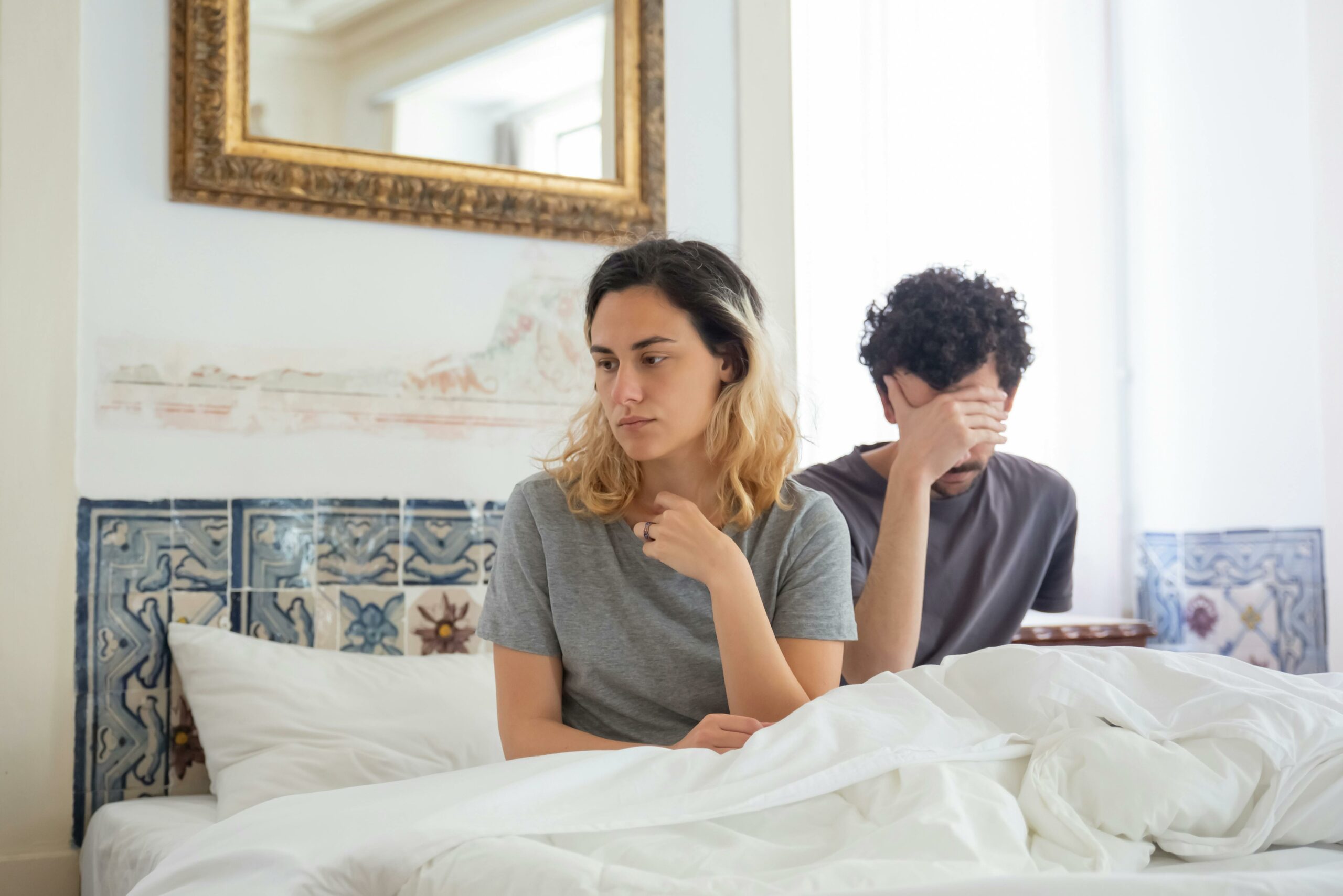 A couple sits together in a bedroom, experiencing a moment of misunderstanding.